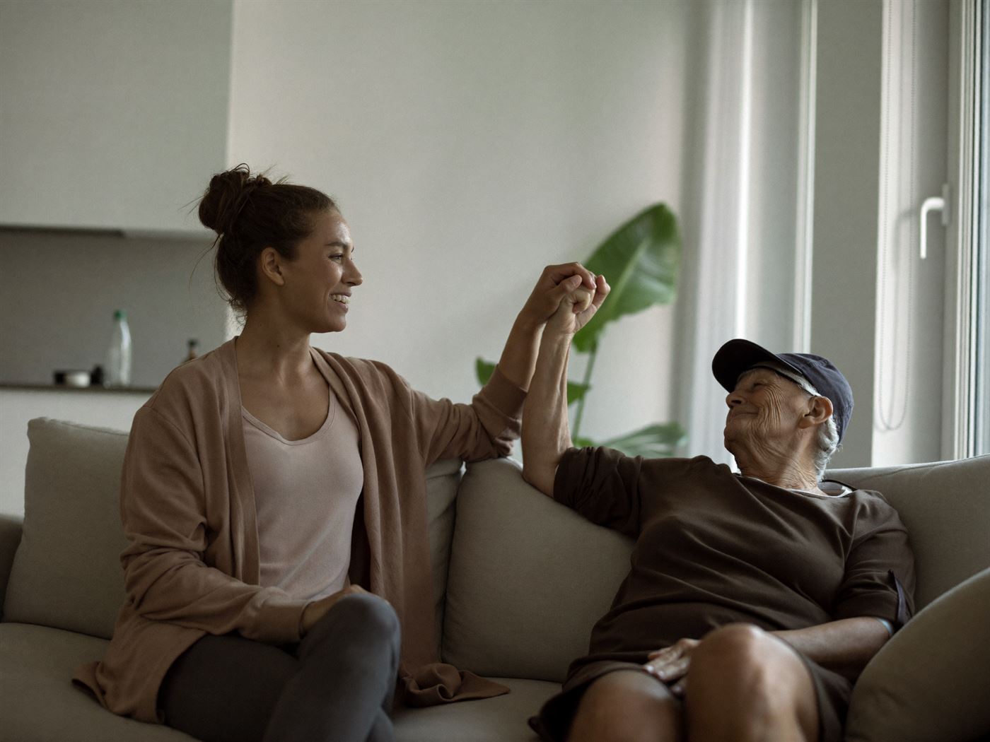 Angehörige sitzt entspannt neben ihrem älteren Vater auf dem Sofa und hält seine Hand
