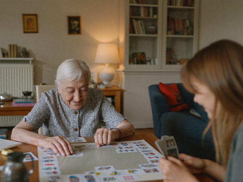 Ältere Dame und Betreuerin spielen gemeinsam ein Gedächtnisspiel am Wohnzimmertisch